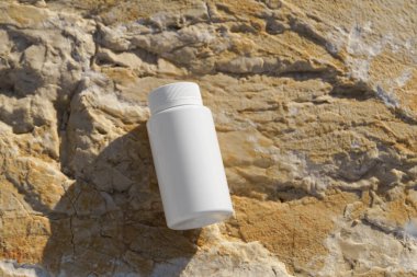 Deniz kenarındaki taşların üzerine beyaz bir takviye kavanozunun kopyası. Doğal sağlık, sağlık, ilaç tedavisi ve bütünsel tedavi kavramı.