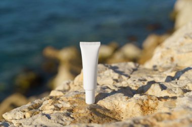 Minimalist beyaz model krem ya da kayalık sahilde okyanus manzaralı losyon tüpü. Güzellik, cilt bakımı ya da spf ve doğal ürün markalaşması ile güneş kremi için mükemmel..