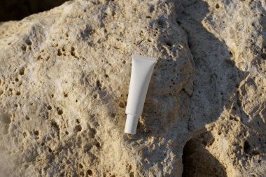 Beyaz krem ya da serum tüpü deniz kenarındaki kireçtaşı taşının üzerinde yatıyor. Doğal güzellik ürünleri, yüz bakımı, nemlendirici ve pürüzsüz cilt kavramı