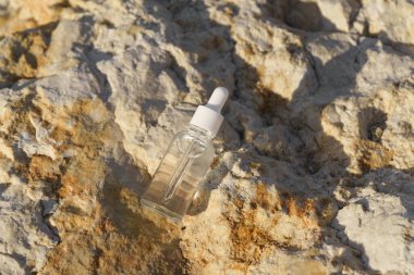 Deniz kenarındaki desenli bir kaya yüzeyine serumu yerleştirilmiş cam damlası şişesi. Doğal nemlendirme serumu cildinizi canlandırır ve besler, kırışıklıkları azaltır.