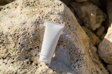 Deniz kenarındaki sünger taşı üzerinde beyaz bir krem tüpü. Yüz ve vücut için doğal kozmetik kavramı, güneş koruması, sağlıklı bronzlaşma.