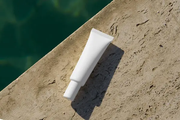 Deniz suyunun yanındaki tuğlada duran beyaz yüz kremi tüpü ya da serum. Güzellik ve estetik kavramı, nemlendirici ve cilt bakım ürünleri, güneş kremi. Tasarımın için resim
