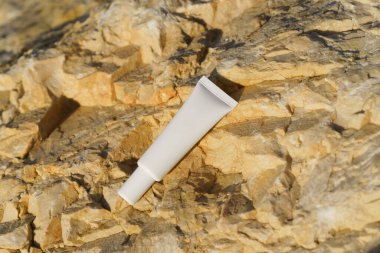 Beyaz krem ya da serum tüpü deniz kenarındaki sarı bir taşın üzerinde yatıyor. Yüz bakımı, güzellik ve estetik ürünleri, cilt suyu ve korunma kavramı