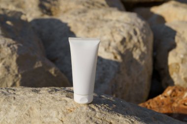 Beyaz model tüp, deniz kenarındaki güneş tarafından aydınlatılan bir taşın üzerinde duruyor. Cilt bakımı kavramı, bronzlaşma için güzellik ürünleri, güneş kremi