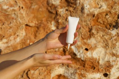 Kadın elleri kireçtaşı zemininde beyaz bir tüp kullanarak serum ya da krem sürerler. Deriyi beslemek ve nemlendirmek için doğal ürünler kavramı, ultraviyole ışınlara karşı koruma