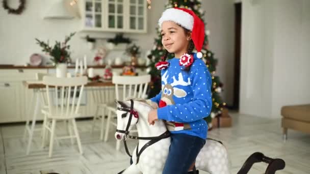파란색 크리스마스 스웨터를 모자를 아프리카 미국인 소녀가 장난감 흔들의자에 크리스마스 — 비디오