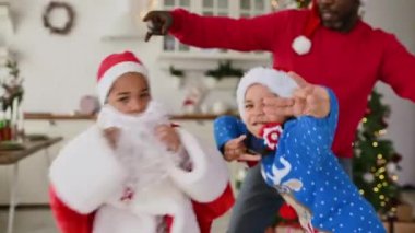 Afrikalı Amerikalı aile - Noel Baba 'nın baba, kız ve oğlu ve sakalı hip hop dansı yapıyor, eğleniyor ve Noel ağacının arka planında sarılıyor..