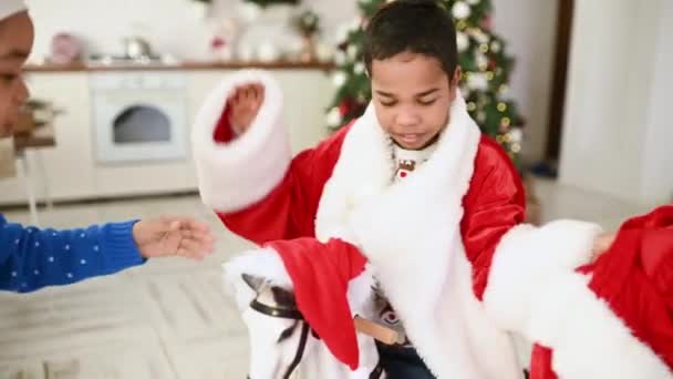 子供たち兄弟姉妹はクリスマスツリーの背景で遊び ロッキングホースに乗って サンタクロースとしてドレスアップし クリスマスを祝う — ストック動画