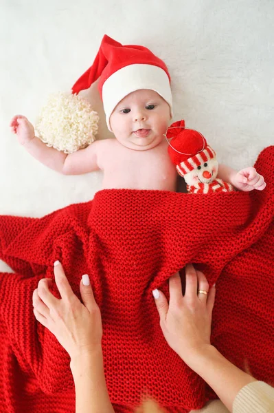 妈妈们用红色毛毯盖住戴着圣诞老人帽子的孩子 孩子手里拿着雪人玩具 — 图库照片