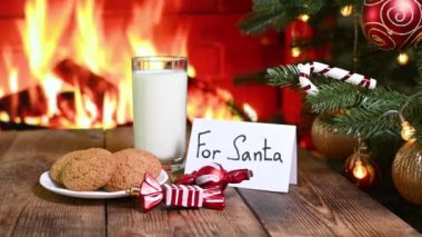 Noel ağacının arka planında bir bardak süt, bir tabak yulaflı kurabiye ve tatlı Noel Baba için bir şömine ve bir tabela.