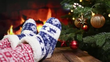 Yılbaşı kırmızı pantolonu ve ev yapımı sıcak çorapları olan, arka planda ren geyiği olan, Noel ağacı ve şöminesi olan bacakları yakın plan.