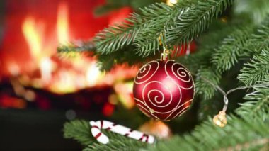 Noel ağacının arka planında kırmızı bir Noel balosu ve yanan şöminede bir ateş..
