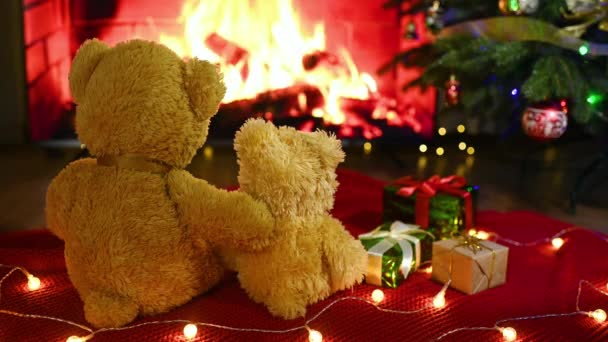 テディベアのカップルは暖炉 贈り物 クリスマスツリーを背景にニットの毛布の上に抱き合って座っています — ストック動画