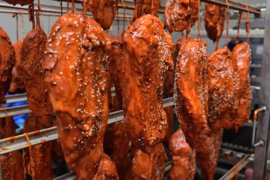 appetizing pieces of pork meat in a tomato marinade sprinkled with sesame seeds hang on a rack against the backdrop of a meat processing plant.
