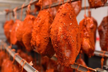 mouth-watering pieces of pork delicacies in paprika and seasonings are hung on a metal rack in a meat-packing plant or butchers shop.