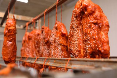appetizing pieces of pork meat in a tomato marinade sprinkled with sesame seeds hang on a rack against the backdrop of a meat processing plant.