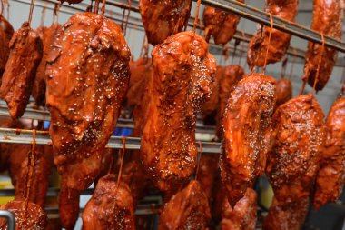 appetizing pieces of pork meat in a tomato marinade sprinkled with sesame seeds hang on a rack against the backdrop of a meat processing plant.