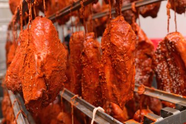 mouth-watering pieces of pork delicacies in paprika and seasonings are hung on a metal rack in a meat-packing plant or butchers shop.