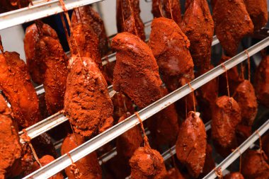 mouth-watering pieces of pork delicacies in paprika and seasonings are hung on a metal rack in a meat-packing plant or butchers shop.