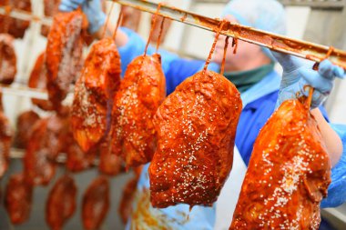 a woman worker of a meat-packing plant hangs appetizing pieces of pork in tomato marinade and sesame on a rack for smoking