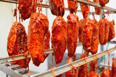 appetizing pieces of pork meat in a tomato marinade sprinkled with sesame seeds hang on a rack against the backdrop of a meat processing plant.