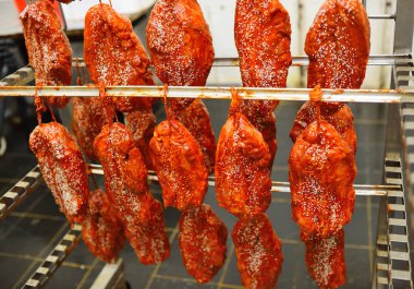 appetizing pieces of pork meat in a tomato marinade sprinkled with sesame seeds hang on a rack against the backdrop of a meat processing plant.