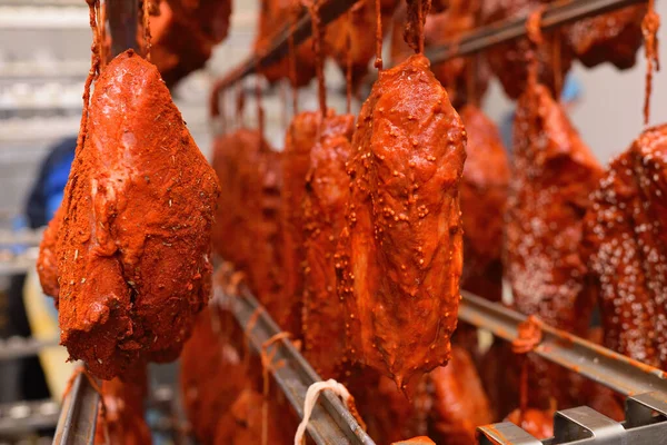 mouth-watering pieces of pork delicacies in paprika and seasonings are hung on a metal rack in a meat-packing plant or butchers shop.