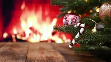 Noel ağacı dallarının arka planına dayalı ahşap bir masa ve şöminede yanan bir ateş..