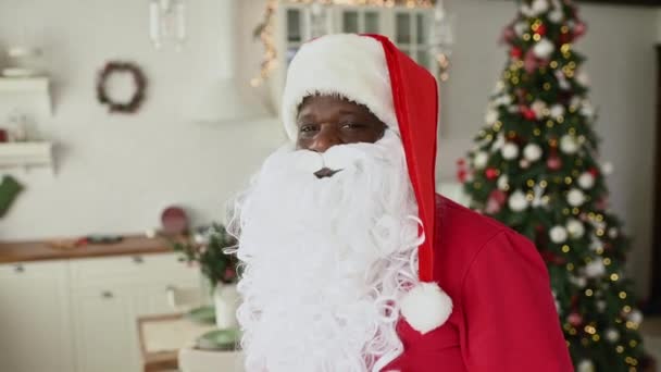 サンタの衣装を着たアフリカ系アメリカ人男性がクリスマスの装飾やモミの木を背景に笑顔で — ストック動画