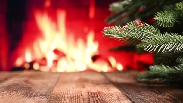 クリスマスツリーの枝や暖炉の燃える火を背景に木製のテーブルのクローズアップ — ストック動画