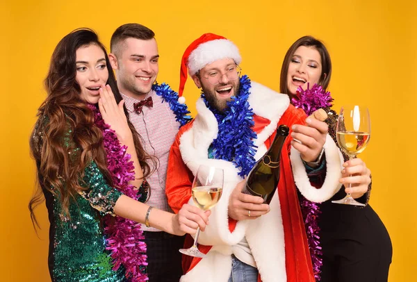 a group or company of friends together with Santa celebrate Christmas, have fun and open champagne holding glasses.