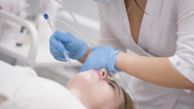 cosmetic procedure gas-liquid peeling - rejuvenation and regeneration of the skin using a jet consisting of oxygen and liquid. The cosmetologist holds an applicator with oxygen and carbon dioxide in