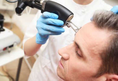 A cosmetologist uses a CO2 fractional ablative laser to rejuvenate the skin of the face and remove vascular asterisks from a male patient in a modern cosmetic beauty clinic.
