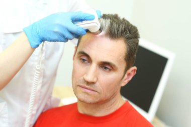 Trichoscopy is a computer examination of the scalp and hair. A cosmetologist-trichologist diagnoses the condition of a male patients hair with gray hair using a trichoscope.