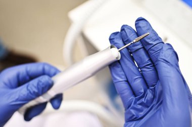 a close-up of a podologist in rubber gloves holding a device with a pedicure drill and a file for the treatment of onychomycosis - a fungal nail disease