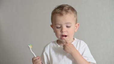Çocuk dişlerini gri bir arka planda diş fırçasıyla fırçalıyor. Ağız temizliği. Pediatrik dişçilik