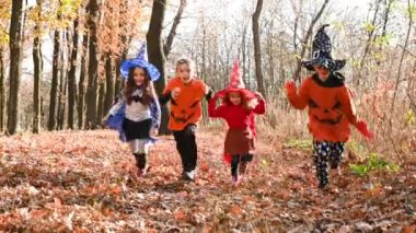 Cadılar Bayramı kostümlü bir grup anaokulu öğrencisi sonbahar ormanının arka planında koşuyor. Azizler Günü Kutlamaları