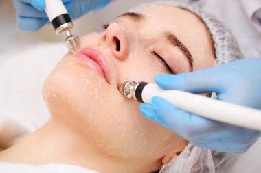 A cosmetologist conducts microcurrent facial therapy for a young woman using a device in a beauty salon. Hardware cosmetology, skin care, rejuvenation, regeneration.