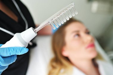 Bir dermatolog trikoloğu, hastaların saçlarının durumunu ve kalitesini iyileştirmek için bu işlemi bir Darsonval cihaz ile gerçekleştirir..