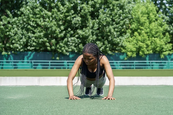 Youth African American woman with long dreadlocks doing push ups exercising outdoors to support athletic body. Ethnic black girl spends free time do fitness alone to improve physical health