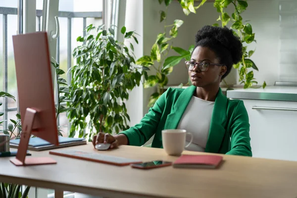 成功したスタートアップの集中アフリカ系アメリカ人女性マネージャーは コンピュータデスクに座っている スタイリッシュな緑のジャケットのビジネス黒の女性は 会社のための投資やバイヤーを見つけるためのプレゼンテーションを準備しています — ストック写真