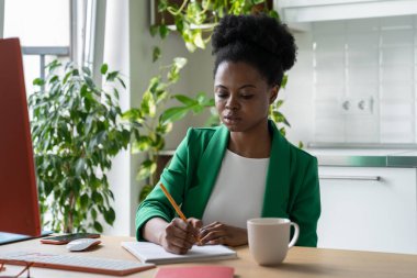 Ev ofisinden çalışan kendine yeten Afrikalı Amerikalı kadın kişisel bilgisayarla masada oturuyor. Başarılı genç siyah kız video yayını ya da iş eğitimi izliyor ve not defterine not tutuyor.