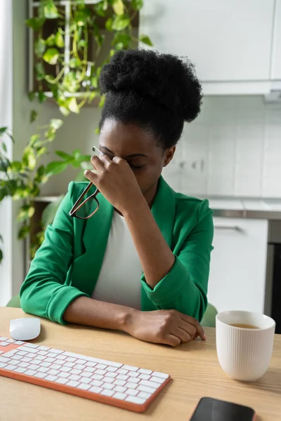 コンピュータで長時間働いた後に目を拭くアフリカ系アメリカ人の女性のフリーランサーは視力の問題を抱えている ビジネス服を着た疲れ切った黒人女性が観葉植物と自宅のオフィスの机に座っています — ストック写真