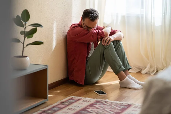 Depressed English Man Sits Floor Own Apartment Sadly Looks Mobile — Stock Photo, Image