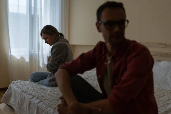 stock image Unhappy family man and woman angry at each other for reasons of misunderstanding or financial problems. Soft focus of young guy and lady sits on opposite sides bed and hesitating to start conversation