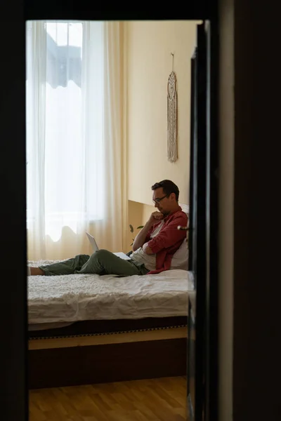 Заботливый Молодой Человек Сидящий Кровати Ноутбуком Коленях Занимается Самообразованием Просматривая — стоковое фото