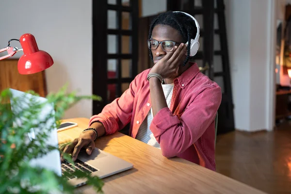 集中した困惑アフリカ系アメリカ人の男性は ノートパソコンを真剣に見て単調で面白い仕事をしています 非アクティブ男は 自宅のオフィスでコンピュータに座っている処理廃棄物の作業時間に苦しんでいます — ストック写真