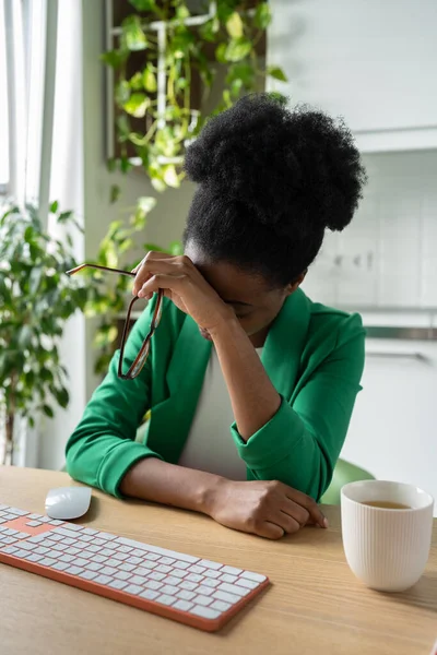 眼鏡をはいたアフリカ人女性は 仕事や残業を強いられた後 手にもたれています キーボードとコーヒーとオフィスの机に座って頭痛を持って疲れビジネスの女の子 バーンアウト — ストック写真