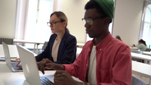 2人は図書館で一緒に勉強しながら ラップトップを使って多人種の学生の男性と女性に焦点を当てた 同僚のスペースでオンラインで働く現代の人々のフリーランス — ストック動画