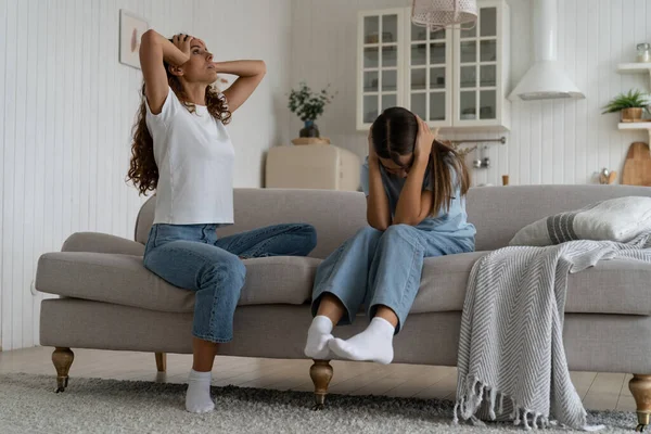 Communication problems between parents and teens. Exhausted parent can not deal with teenage daughter attitude, parental burnout. Teen girl covering ears with hands not to listen mom, sitting on sofa